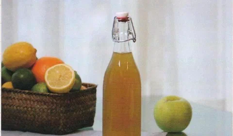 Berro en almíbar, embotellado, junto a una canasta de cítricos y una manzana