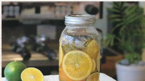 Mandarina y naranja en almíbar, embotellado, junto a un limón cortado por la mitad