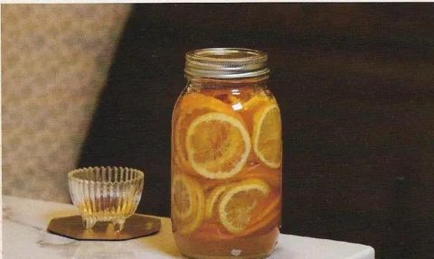 Naranja y limón en almíbar, embotellado, junto a una copa pequeña de almíbar servido