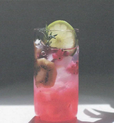 Ade de flor de jamaica y lima, de un rojo intenso, con kiwi, granada y una rodaja de limón