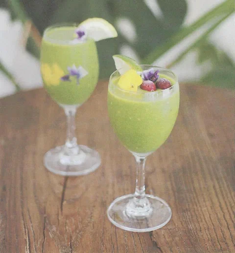 Smoothie verde de primavera, decorado con piña, flores comestibles y arándanos rojos