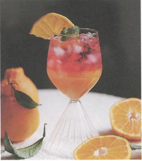 Ade de mandarina pelada y flor de jamaica, en copa, con rodaja de naranja y menta de decoración