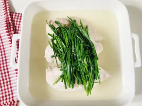 Pechuga de pollo baeksuk en su caldo, cubierta con cebolla china o chalotas verdes