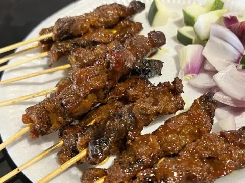Brochetas de pechuga de pollo sate, doradas y servidas con cebolla morada y pepino