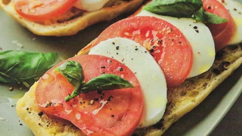 Sándwiches abiertos de pan de aceitunas con mozzarella fresca, tomate y albahaca