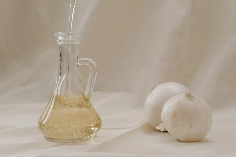 Aceite de oliva sirviéndose en una aceitera de vidrio, junto a bulbos de ajo