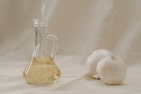 Aceite de oliva sirviéndose en una aceitera de vidrio, junto a bulbos de ajo