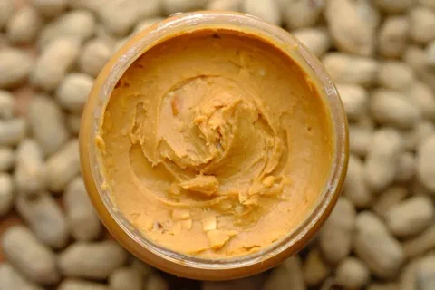 Mantequilla de maní en un frasco abierto, con maníes alrededor