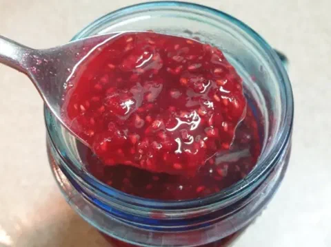 Compota de frambuesa en un frasco, con una cuchara mostrando la textura espesa