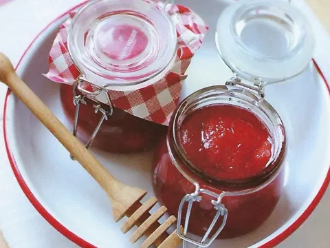 Frascos de compota de fresa con una cuchara de madera al costado