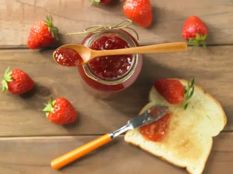 Mermelada de fresa y rosas untada sobre una tostada, con fresas al costado