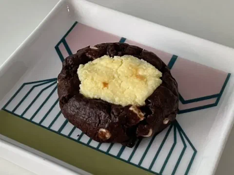 Galleta de chocolate y queso crema, cubierta de chips de chocolate, con el centro cremoso asomando