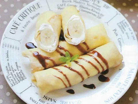 Dos crepes enrollados alrededor de un plátano entero, bañados en salsa de chocolate, con menta como decoración