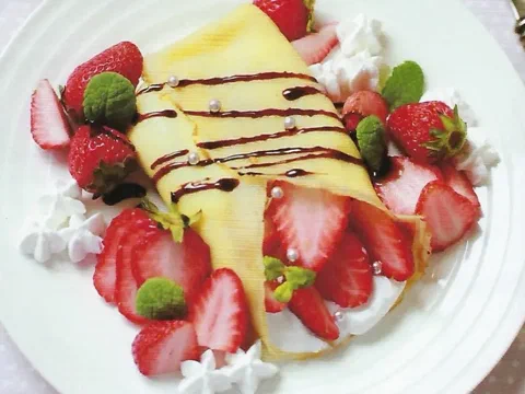 Crepe doblado en sobre, relleno de crema batida y fresas frescas, decorado con salsa de chocolate