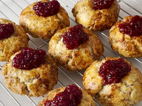 Scones de frambuesa y crumble sobre una rejilla, con la mermelada visible en el centro