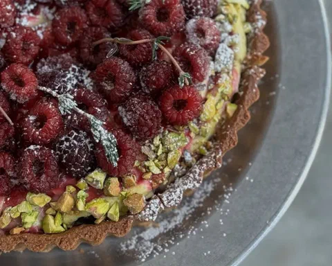 Tarta de pistacho y frambuesa, cubierta de frambuesas frescas, pistacho picado y azúcar impalpable
