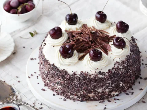 Torta selva negra cubierta de chocolate rallado, decorada con cerezas frescas y virutas de chocolate
