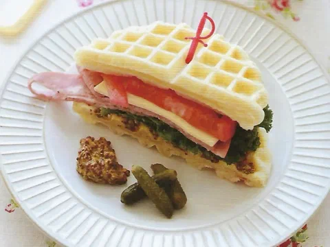 Sándwich hecho con dos discos de waffle, relleno de jamón, tomate, queso y hojas verdes