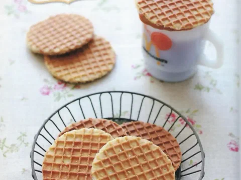 Stroopwafels apilados junto a una taza, con uno reposando encima como cobertura de la bebida